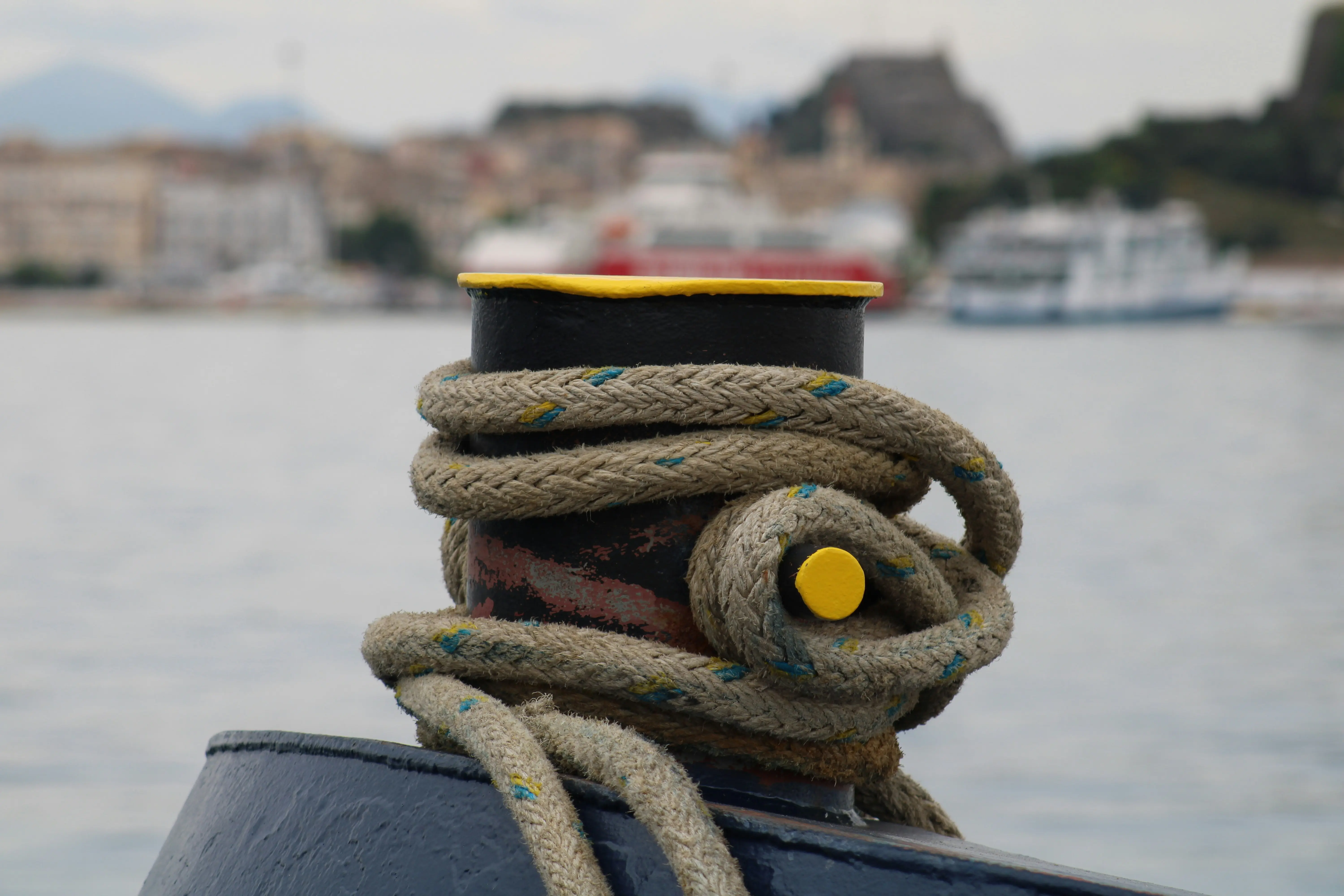 Thick rope coiled around a bollard with harbor in background